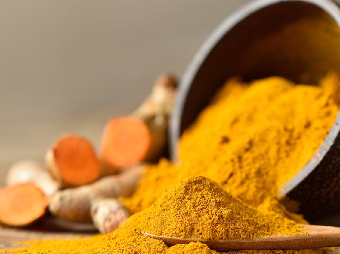 Ground turmeric spilling from a bowl with fresh turmeric roots in the background.