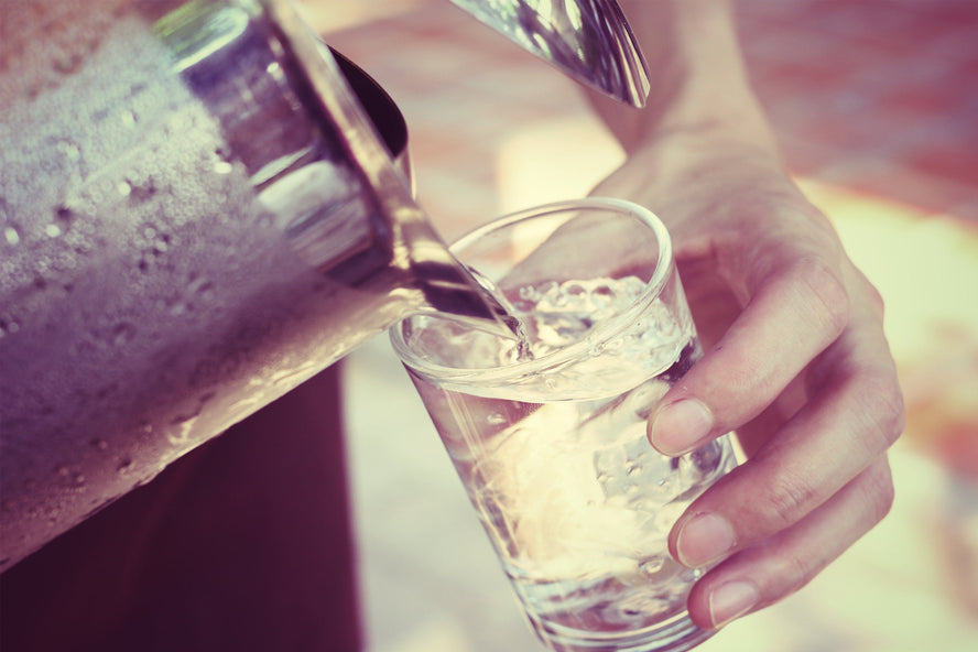 A glass of ice water poured from a silver picture with a woman’s hand holding the glass