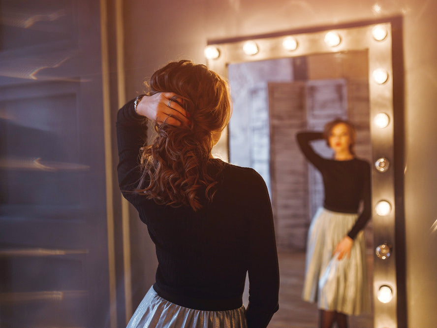 Woman in party dress holding up her beautiful hair while gazing into a full-length mirror