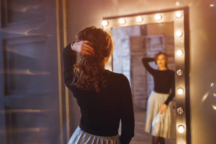 Woman in party dress holding up her beautiful hair while gazing into a full-length mirror