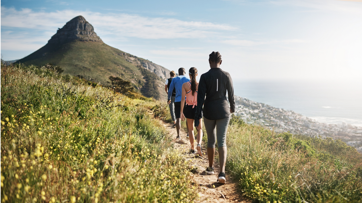 Group hiking on a mountain trail with a wide scenic view of mountains and sky.